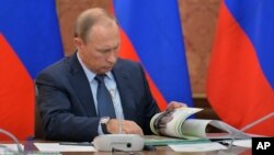 FILE - Russian President Vladimir Putin looks through a book during meeting with senior government officials in Magas, regional Ingushetian capital, Russia, Sept. 13, 2015.