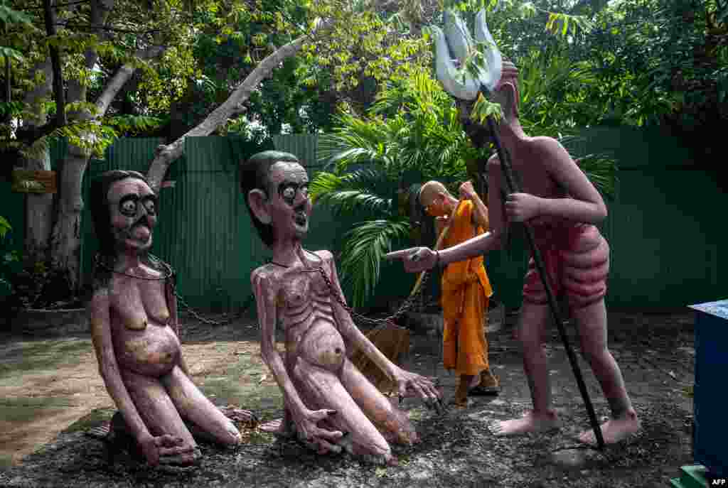 A Buddhist monk cleans the area around statues demonstrating the fate of people who do bad things, in a garden representing a Buddhist version of hell at the Wat Saeng Suk temple, in the Thai coastal area of Chonburi, Thailand.