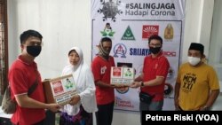 Dua orang warga menerima paket sembako. Mereka adalah warga terdampak corona yang masuk dalam golongan pekerja informal. (Foto: VOA/Petrus Riski)