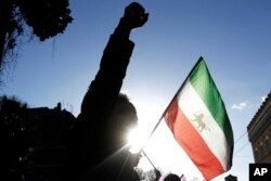 A demonstrator shouts slogans near the flag of the former Imperial State of Iran as he gathers with supporters of Maryam Rajavi, head of the Iranian opposition group National Council of Resistance, outside the Iran Embassy, in Rome, Jan. 2, 2017.