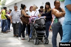A mother takes care of her daughter while lining up outside a drugstore to buy diapers in Caracas, July 21, 2015.