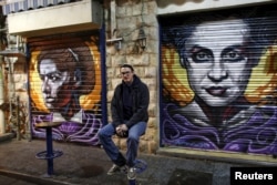 Artist Solomon Souza poses for a picture near portraits he spray-painted on metal shutters of closed storefronts in Mahane Yehuda, one of Jerusalem's most popular outdoor markets, Feb. 24, 2016.