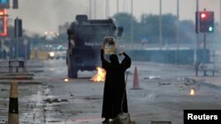 FILE - A female protester holds a photo of Shi'ite scholar Isa Qassim as she confronts riot police armoured personnel carrier during a demonstration to mark the 6th anniversary of the February 14 uprising, in the village of Sitra, south of Manama.