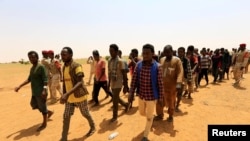 FILE - Migrants from Ethiopia, Sudan and Chad, who were abandoned by traffickers in a remote desert area near the Libyan border, walk after being arrested by Sudan's paramilitary Rapid Support Forces on the Khartoum State border, Sudan, Sept. 25, 2019.