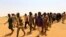 FILE - Migrants from Ethiopia, Sudan and Chad, who were abandoned by traffickers in a remote desert area near the Libyan border, walk after being arrested by Sudan's paramilitary Rapid Support Forces on the Khartoum State border, Sudan, Sept. 25, 2019.
