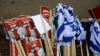 Israeli flags lie on the ground with signs showing the faces of Israeli Prime Minister Benjamin Netanyahu (R) and ex-rival Benny Gantz (L) with a caption in Hebrew reading 'Israeli ashamed' during a May 14, 2020, demonstration against the new government.