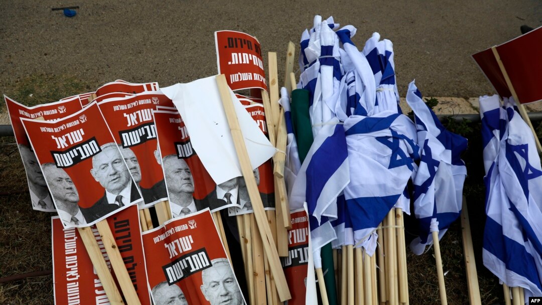 Israeli flags lie on the ground with signs showing the faces of Israeli Prime Minister Benjamin Netanyahu (R) and ex-rival Benny Gantz (L) with a caption in Hebrew reading 'Israeli ashamed' during a May 14, 2020, demonstration against the new government.