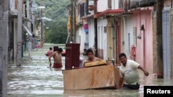Ljudi nose nameštaj kroz poplavljene ulice u gradiću Tikstla 