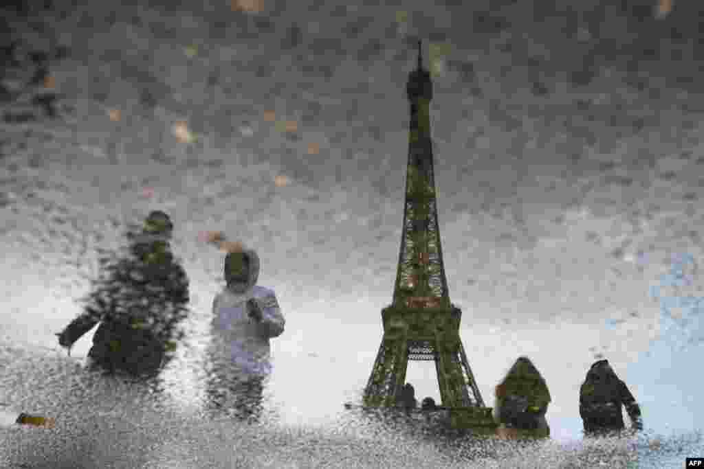 This photograph shows the reflection of tourists walking past the Eiffel Tower in Paris, France.