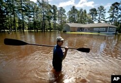 The home of Kenny Babb is surrounded by water as he retrieves a paddle that floated away while the Little River continues to rise in the aftermath of Hurricane Florence in Linden, North Carolina, Sept. 18, 2018.