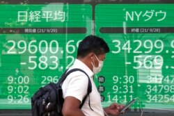 A man wearing a protective mask walks in front of an electronic stock board showing Japan's Nikkei 225 and New York Dow indexes at a securities firm, Sept. 29, 2021, in Tokyo.