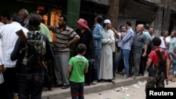 FILE - Rebel fighters stand guard as people queue for bread in the rebel held al-Shaar neighborhood of Aleppo, Syria, July 14, 2016. 