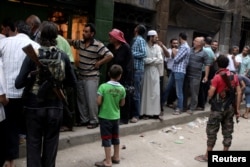 Rebel fighters stand guard as people queue for bread in the rebel held al-Shaar neighborhood of Aleppo, Syria July 14, 2016.