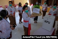 Petugas pemilu memakai masker pelindung saat pemilihan kepala daerah di Denpasar, Provinsi Bali, 9 Desember 2020. (Foto: Antara/Fikri Yusuf via REUTERS