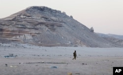 FILE - In this photo taken March 6, 2017, a Somali government soldier walks on the beach in Eyl, in Somalia's semiautonomous northeastern state of Puntland.