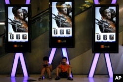 2017年8月10日，孩子们在北京一家电影院显示电影《战狼2》的电子屏幕附近使用手机，美联社提供。