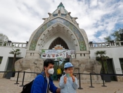 Seorang anak laki-laki menunjukkan kartu vaksinasi COVID-19, didampingi ayahnya saat mengunjungi Kebun Binatang Budapest, di Budapest, Hungaria, 1 Mei 2021. (AP)