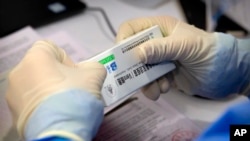 A worker opens a package of coronavirus vaccine made by a Sinopharm subsidiary during a COVID-19 vaccination session for resident foreign journalists at a vaccination center in Beijing, Tuesday, March 23, 2021. 