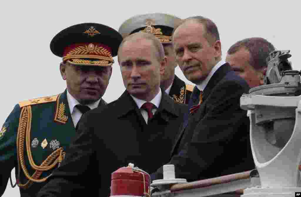 Russian President Vladimir Putin, flanked by Defense Minister Sergei Shoigu, left, and Federal Security Service Chief Alexander Bortnikov, right, arrives on a boat after inspecting battleships during a navy parade marking the Victory Day in Sevastopol, Crimea, May 9, 2104.