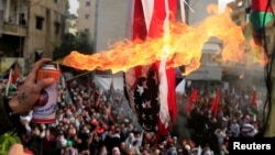 Des manifestants mettent le feu à un drapeau des États-Unis près de l'ambassade des États-Unis à Awkar, au nord de Beyrouth, au Liban, le 10 décembre 2017.