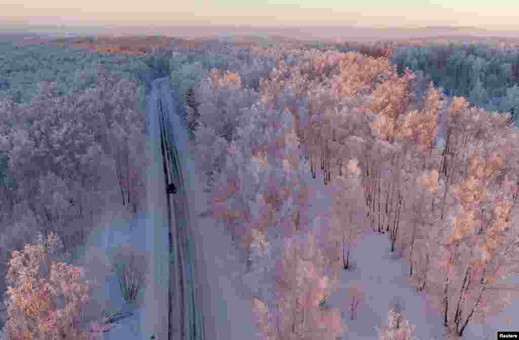 تصویری از رانندگی در امتداد جاده جنگلی پوشیده از برف به هنگام غروب آفتاب در روسیه &nbsp;