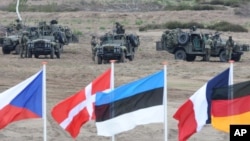FILE - Flags wave in front of soldiers taking positions with their army vehicles during the NATO Noble Jump exercise on a training range near Swietoszow Zagan, Poland, June 18, 2015.