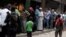 FILE - Rebel fighters stand guard as people queue for bread in the rebel held al-Shaar neighborhood of Aleppo, Syria, July 14, 2016. 