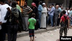 Rebel fighters stand guard as people queue for bread in the rebel held al-Shaar neighborhood of Aleppo, Syria July 14, 2016. 