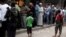 Rebel fighters stand guard as people queue for bread in the rebel held al-Shaar neighborhood of Aleppo, Syria July 14, 2016. 