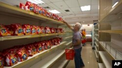 FILE - A man takes a package of cookies surrounded by empty shelves of a supermarket in Caracas, Venezuela, March 23, 2018. 