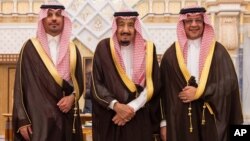 In this photo provided by the Saudi Press Agency, the new Economy and Planning Minister, Mohammad al-Tuwaijri, right and the new National Guard chief, Prince Khalid bin Ayyaf al-Muqrin, left, pose for a photo with King Salman during a swearing in ceremony, in Riyadh, Saudi Arabia, Nov. 6, 2017. The king has sworn in new officials to take over from a powerful prince and former minister believed to be detained in a large-scale sweep that has upended longstanding traditions. 