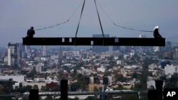 Trabajadores de la construcción viajan sobre una viga que cuelga de una grúa en el sitio de construcción de un edificio residencial de gran altura en la Ciudad de México, el 17 de junio de 2022.