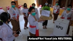 Petugas pemilu memakai masker pelindung saat pemilihan kepala daerah di Denpasar, Provinsi Bali, 9 Desember 2020. (Foto: Antara/Fikri Yusuf via Reuters)