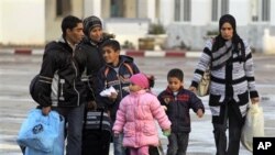 Members of a Tunisian family carry their belongings after they fled from Libya, at the Tunisia-Libya border near the village of Ras Ajdir, Tunisia, Wednesday, Feb. 23, 2011