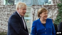 FILE - German Chancellor Angela Merkel, right, greets Britain's Prime Minister Boris Johnson upon his arrival for a meeting at the Chancellery in Berlin, Jan. 19, 2020.