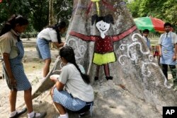 FILE - Indian schoolgirls paint a tree trunk at a park to mark Earth Day in Kolkata, April 22, 2017.