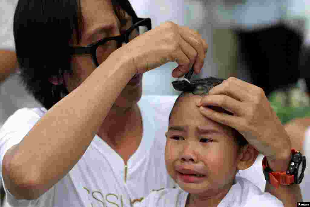 A devotee girl has her hair shaved by her father during a mass ceremony to mark the first anniversary of late Thailand&#39;s King Bhumibol Adulyadej&#39;s death, at the Sathira-Dhammasathan Buddhist meditation center in Bangkok.