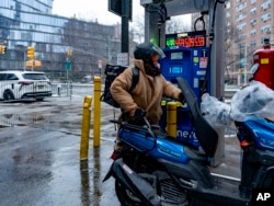 A man dispenses gasoline into a moped at a Mobil station on Friday, Jan. 19, 2024, in New York. (AP Photo/Peter K. Afriyie)
