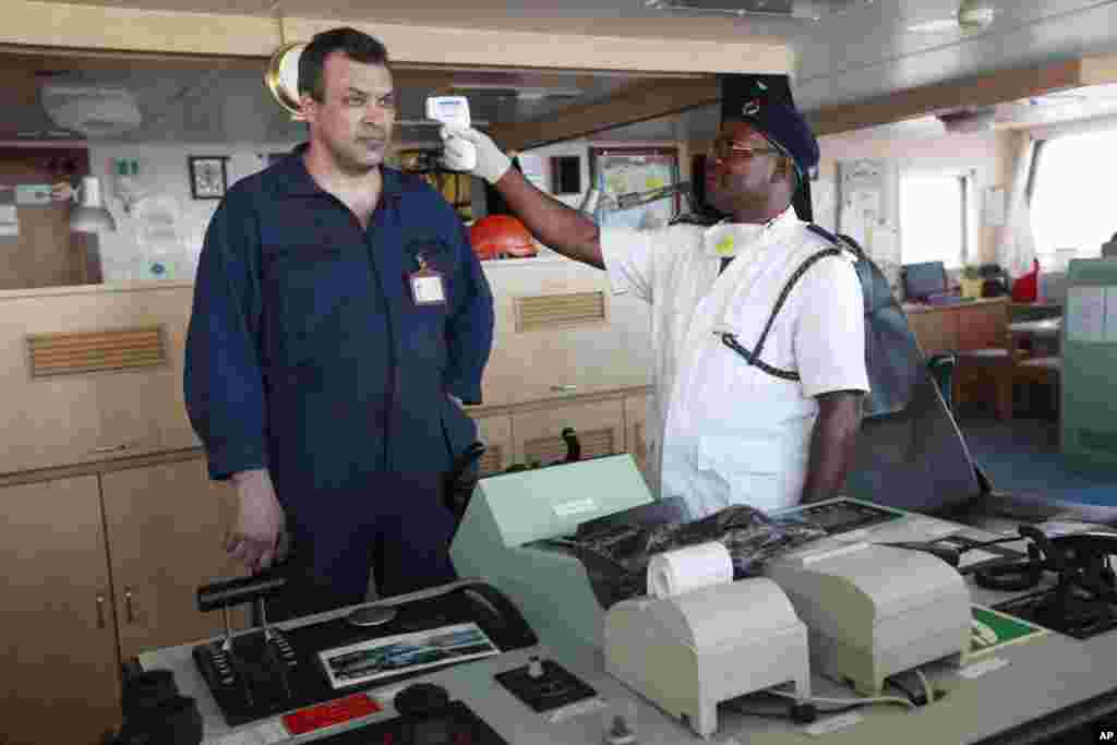 A Nigerian port health official uses a thermometer to screen a Ukrainian captain, Bosenko Rusian,&nbsp; for Ebola, on the deck of a cargo ship at the Apapa port, in Lagos, Nigeria, Sept. 29, 2014. 