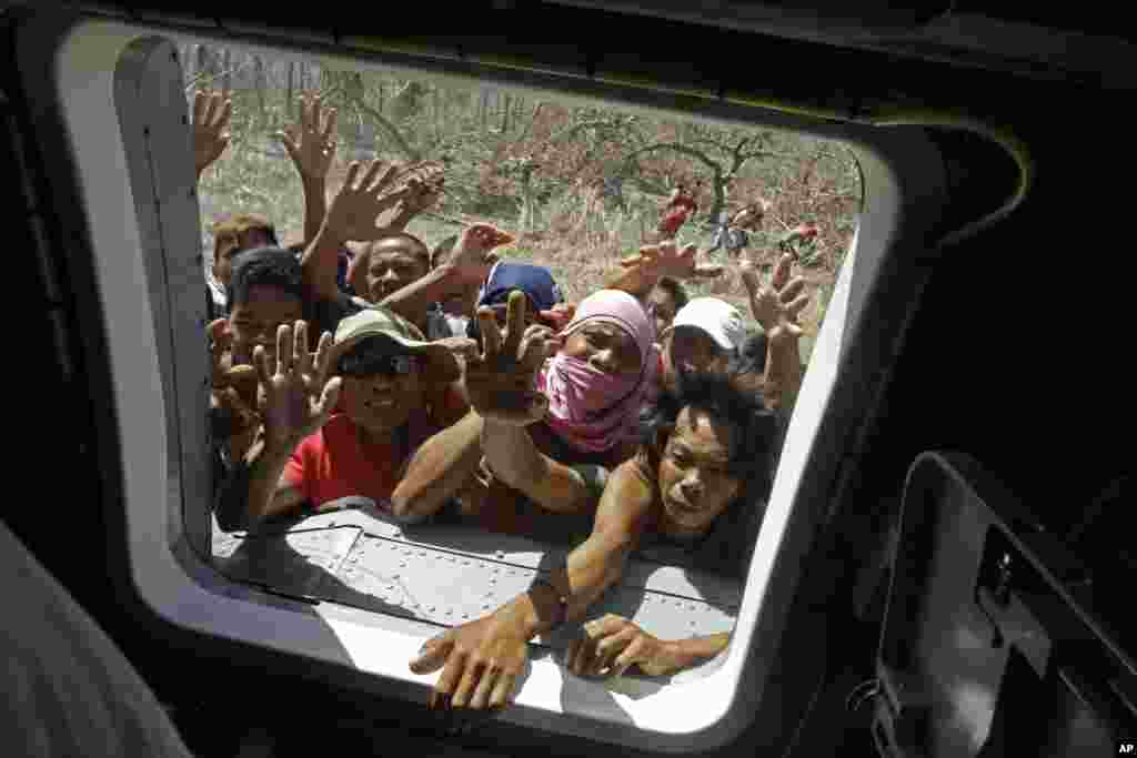 People rush to a window of a U.S. Navy Seahawk helicopter as crewmen deliver aid in an emergency drop in San Jose, Philippines, Nov. 18, 2013. 