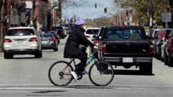A woman wears a protective mask and gloves, due to the COVID-19 virus outbreak, as she bicycles through busy traffic in Lawrence, Mass., May 5, 2020. Massachusetts Gov. Charlie Baker in April encouraged people to remain home until at least May 18th.