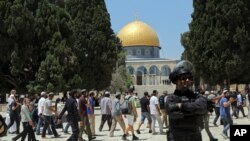 An Israeli police officer stands guard as Jewish men visit the Dome of the Rock Mosque in the Al Aqsa Mosque compound, during the annual mourning ritual of Tisha B'Av, in Jerusalem's Old City, July 18, 2021.