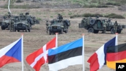 FILE - Flags wave in front of soldiers taking positions with their army vehicles during the NATO Noble Jump exercise on a training range near Swietoszow Zagan, Poland, June 18, 2015.