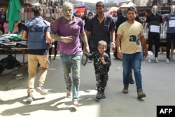 A man with his face covered in dust walks alongside a child through a commercial street following an Israeli strike in the Shujaiya neighborhood of Gaza City on Sept. 18, 2024.