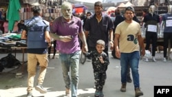 (FILE) A man with his face covered in dust walks alongside a child through a commercial street following an Israeli strike in Gaza City on September 18, 2024.