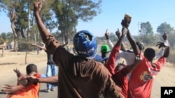 A rioter wearing a police helmet taken from a police officer joins angry protesters in Harare, Monday, July, 4, 2016. Police in Zimbabwe's capital fired tear gas and water cannons in an attempt to quell rioting by taxi and mini bus drivers protesting what they describe as police harassment. (AP Photo/Tsvangirayi Mukwazhi)