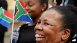 People hold South African flags as Nelson Mandela Foundation CEO Sello Hatang speaks to the press on the steps of the Johannesburg High Court, Aug. 21, 2019, after South Africa's Equality Court restricted the display of the old apartheid-era flag.