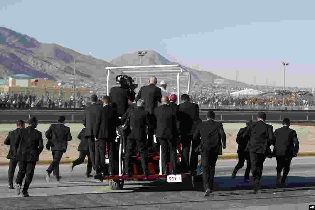Security guards run alongside the popemobile transporting Pope Francis to a ramp near the Mexican-U.S. border fence, where he offered a prayer for migrants, in Ciudad Juarez, Mexico, Feb. 17, 2016.
