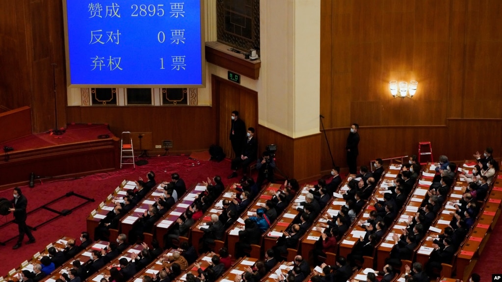 在北京人民大会堂举行的全国人民代表大会闭幕会议上，代表们在屏幕旁鼓掌，屏幕上显示了支持赋予亲北京的委员会权力以任命更多香港立法会议员的投票数。(2021年3月11日)(photo:VOA)