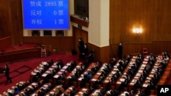 在北京人民大会堂举行的全国人民代表大会闭幕会议上，代表们在屏幕旁鼓掌，屏幕上显示了支持赋予亲北京的委员会权力以任命更多香港立法会议员的投票数。(2021年3月11日)